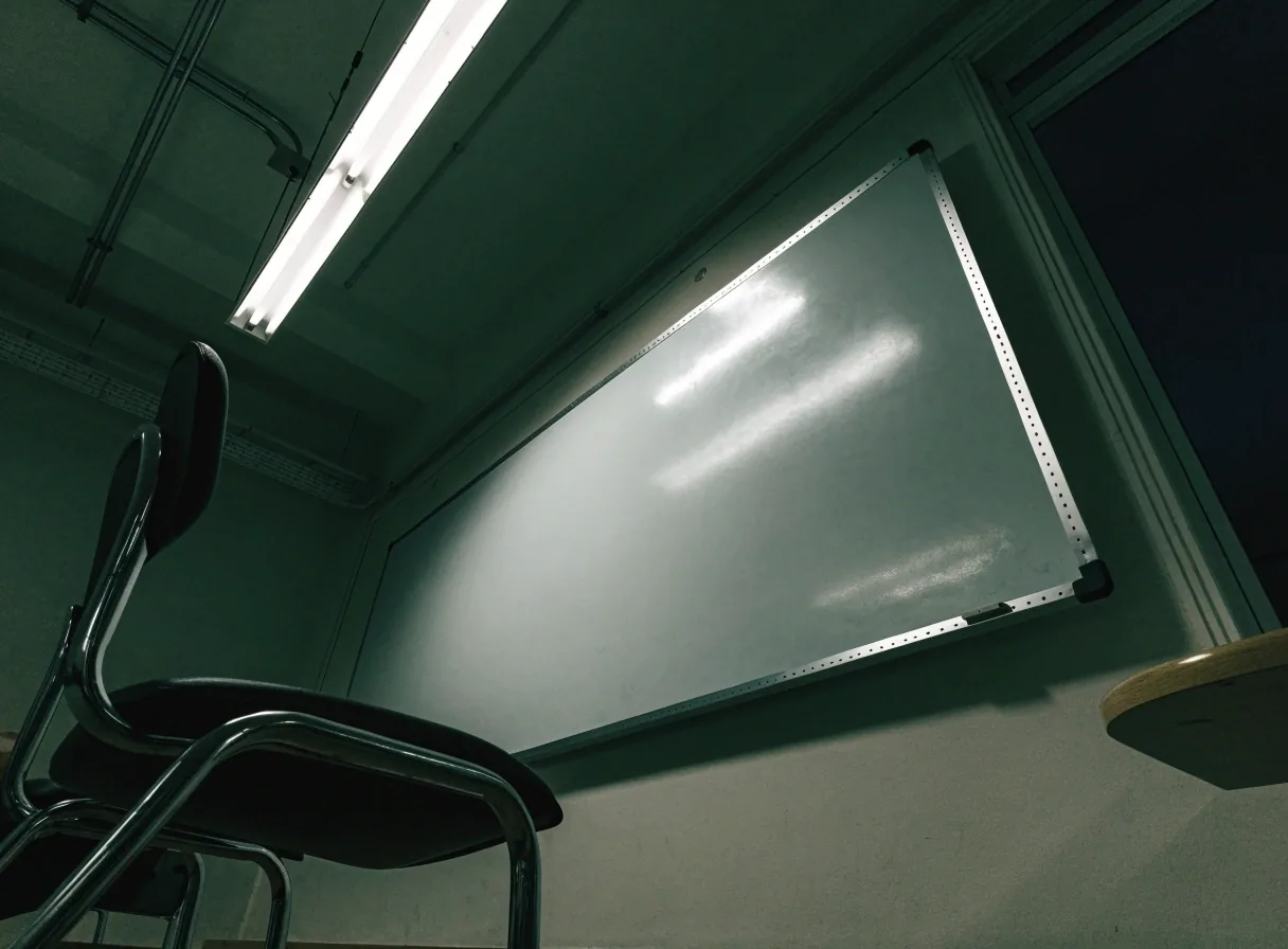An unmarked whiteboard and a single chair in a classroom photographed at night